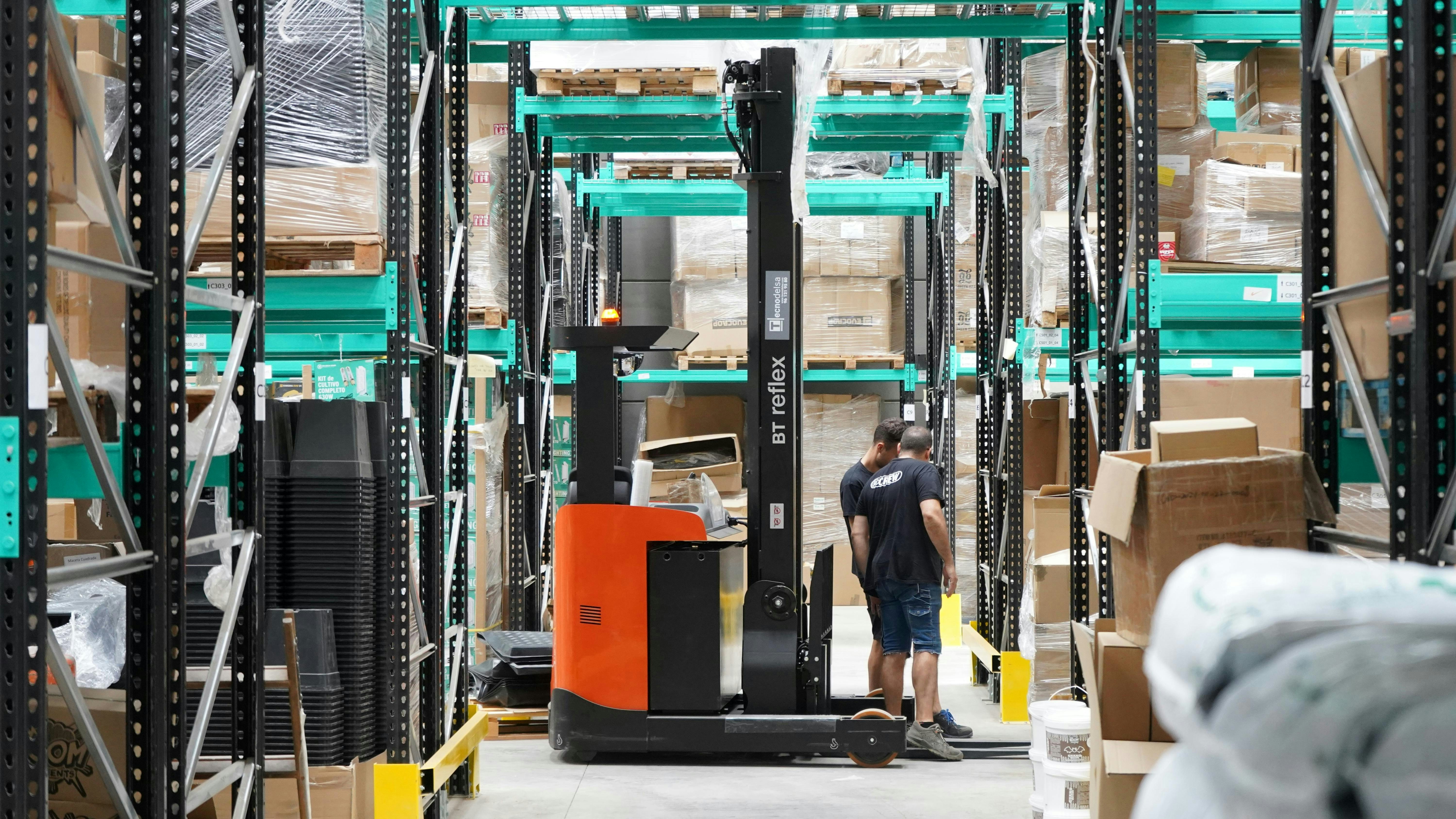 Operator met reach-truck tussen groene magazijnracking